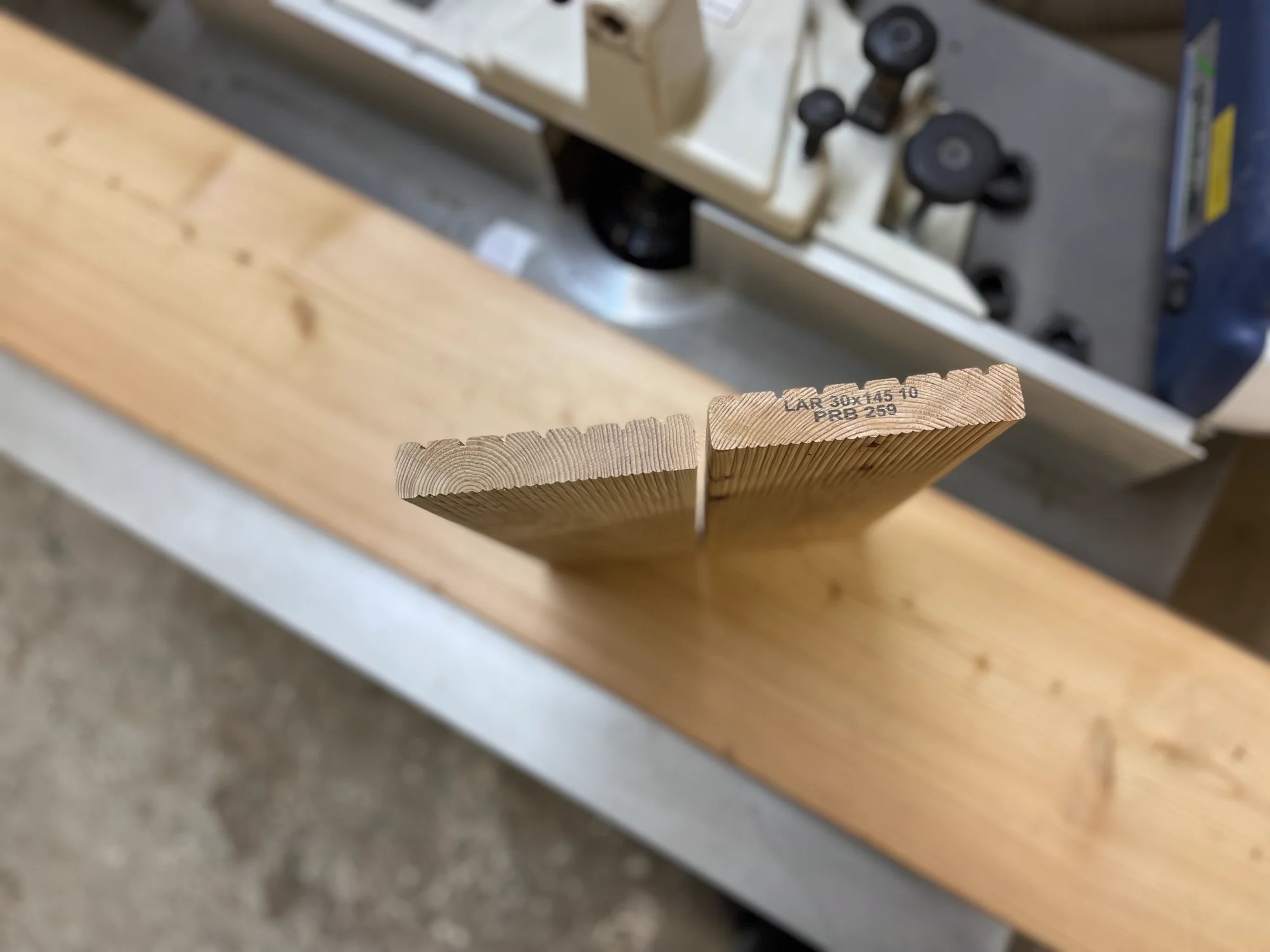 Hochkant aufgestelltes Brett mit ausgearbeiteten Zapfen vor einer Holzbearbeitungsmaschine in der Werkstatt