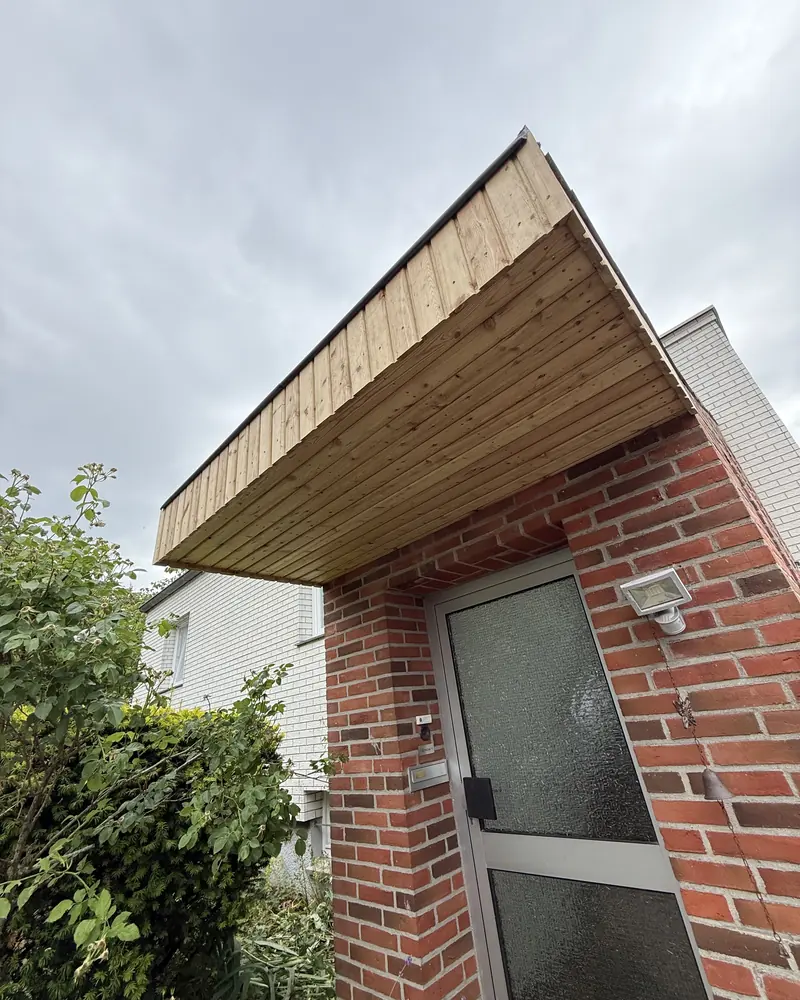 Auskragendes Vordach von unten, die Holzschalung zeichnet sich gegen den Himmel ab