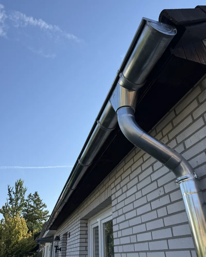 Neue Zinkdachrinne mit Fallrohr an einem Klinkerhaus vor blauem Himmel