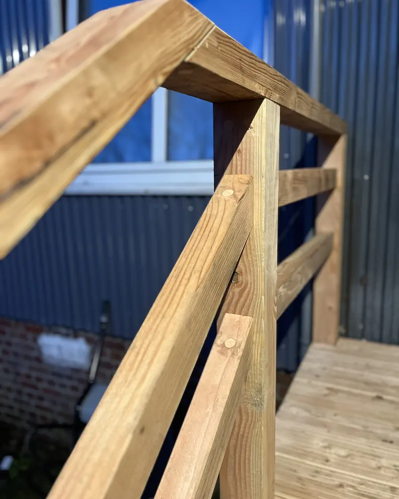 Detail eines Holzgeländers mit Pfosten, Handlauf und angeschrägter Strebe